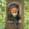 Small garden gnome statue peeking from arched metal window, green shirt and blue pants
