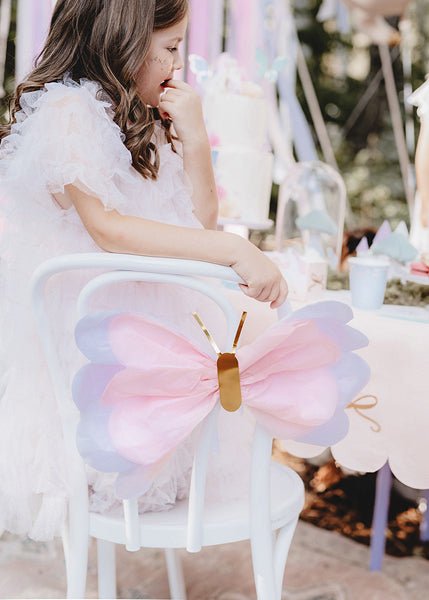 Pink tissue paper butterfly hanging decor with gold center, shown on a chair near a child